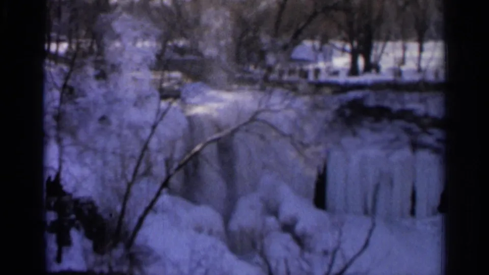 1966 Hamel, Minnesota home-movie frame of icy waterfall formations, snowy ground, bare trees, and indistinct people in the background.