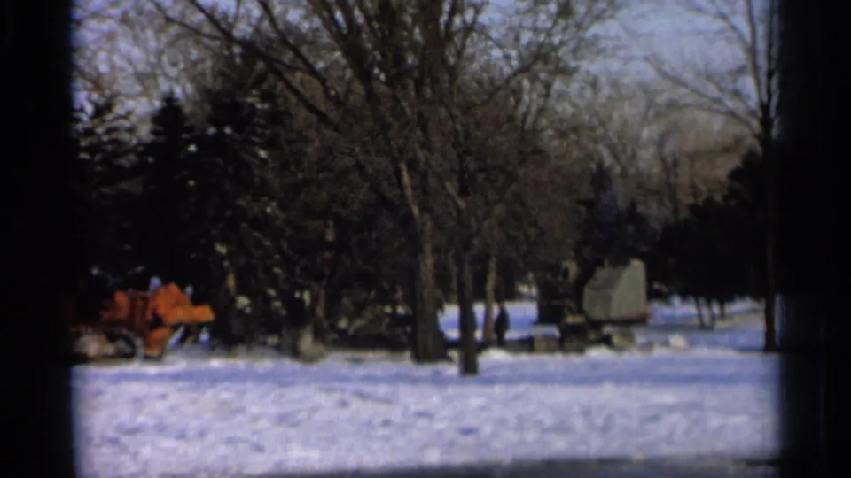 1966 Hamel, Minnesota home-movie frame showing orange winter machinery near trees on snow-covered ground.