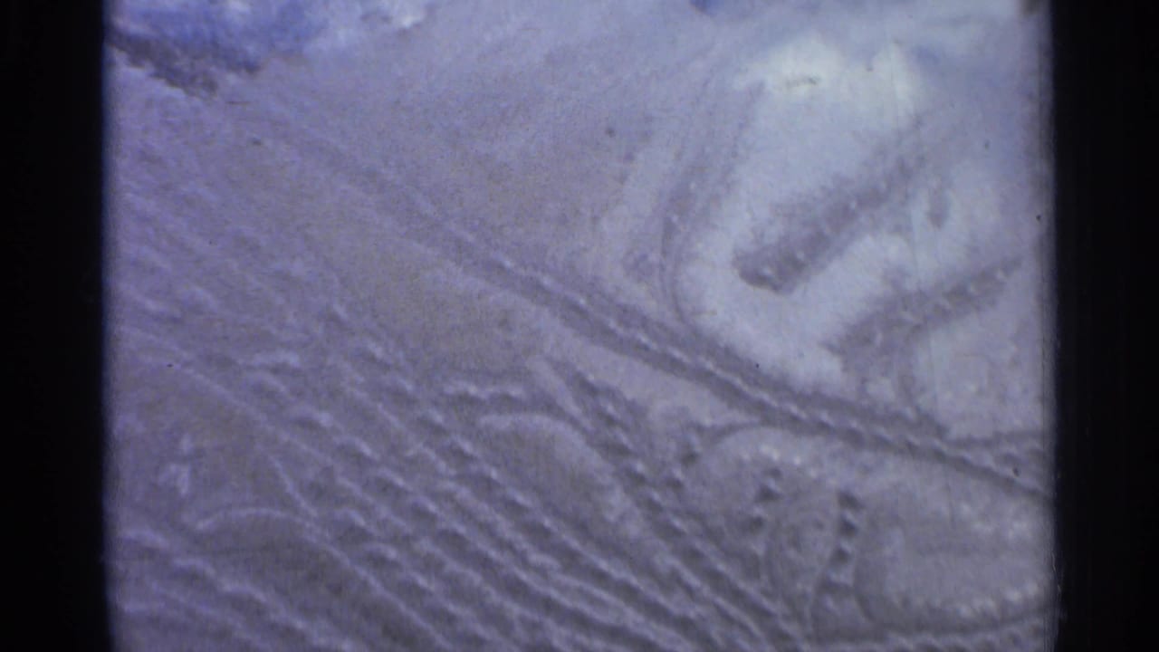 Close view of snowmobile tracks pressed into snowy ground with dark debris nearby.