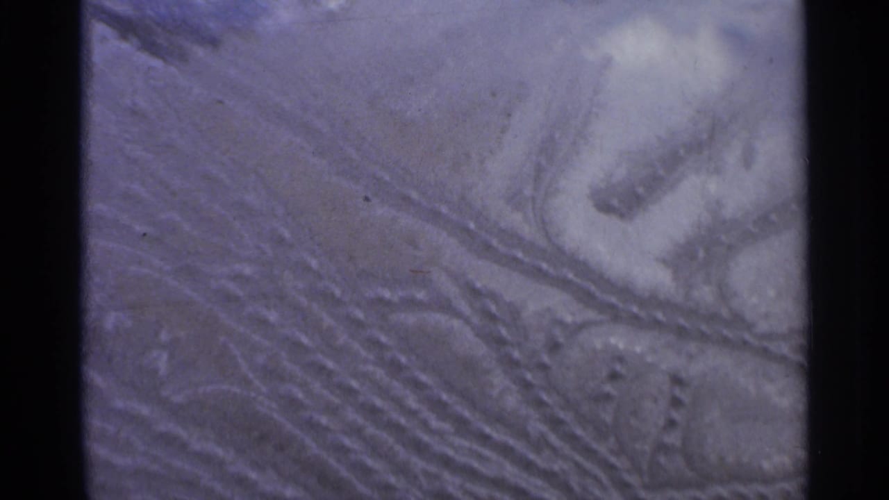 Snow surface with repeated track grooves, compacted patches, and small dark marks.
