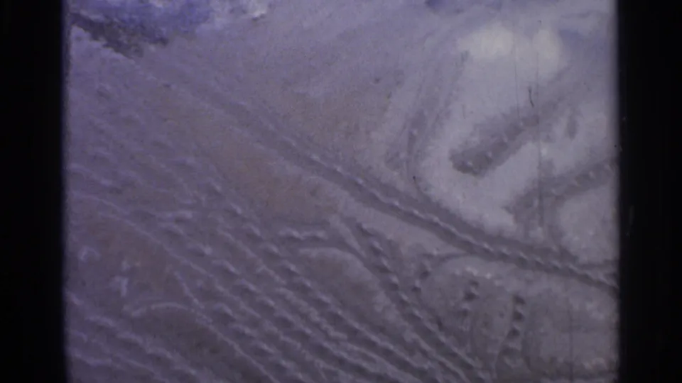 Vintage 8mm frame from 1966 Hamel showing curved snowmobile track impressions across textured winter snow.