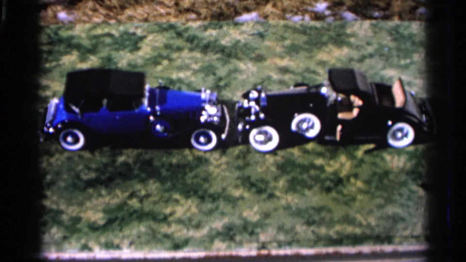 The blue convertible and black roadster remain parked on grass in this 1966 Hamel, Minnesota home-movie frame.