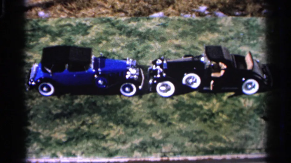 Final 1966 Hamel, Minnesota frame of two classic open-top cars parked on grass, with whitewall tires and chrome visible.