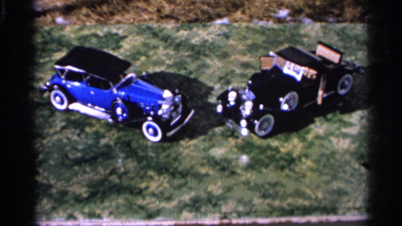 1966 Hamel, Minnesota 8mm frame showing a blue convertible and black touring car parked side by side on grass.