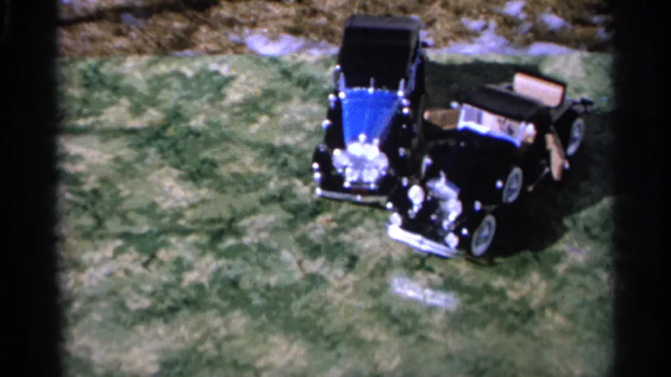 Two remotely controlled toy cars sit close together on a grassy lawn in 1966 Hamel, Minnesota home-movie footage.