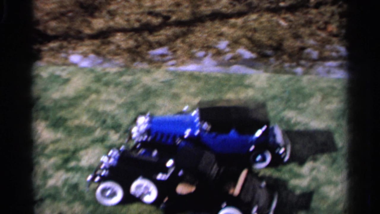 Blue toy car on grass beside dark film-frame borders.