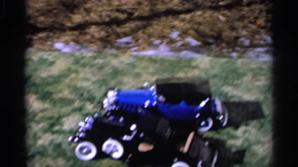 A blue toy car sits or moves across grass in 1966 Hamel, Minnesota home-movie footage, framed by dark film edges.
