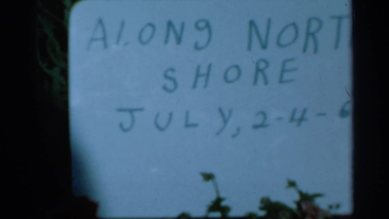 1966 8mm home-movie frame showing a handwritten Along North Shore title card with July dates, partly obscured at the edge.