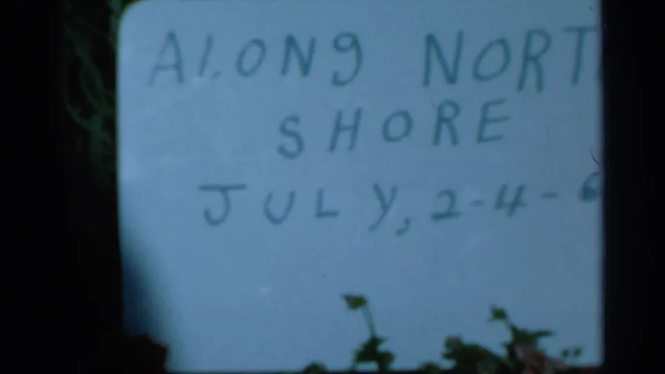 1966 8mm home-movie frame showing a handwritten Along North Shore title card with July dates, partly obscured at the edge.