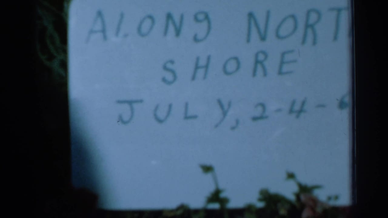 Second view of the handwritten Along North Shore sign with July dates in soft focus.