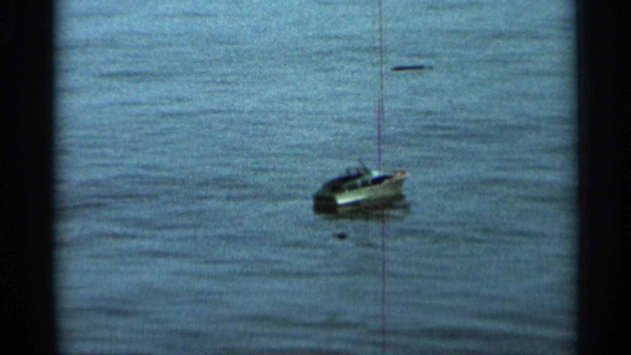 Small toy sailboat seen farther right on calm lake water.