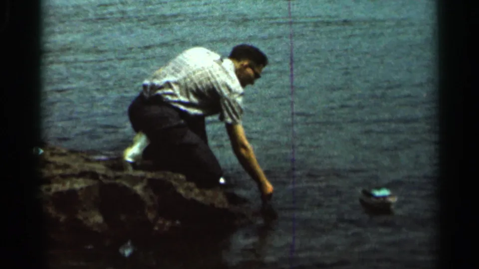 In 1966 Hamel, Minnesota home-movie footage, a man kneels at a rocky lake edge and sets a small toy boat afloat.