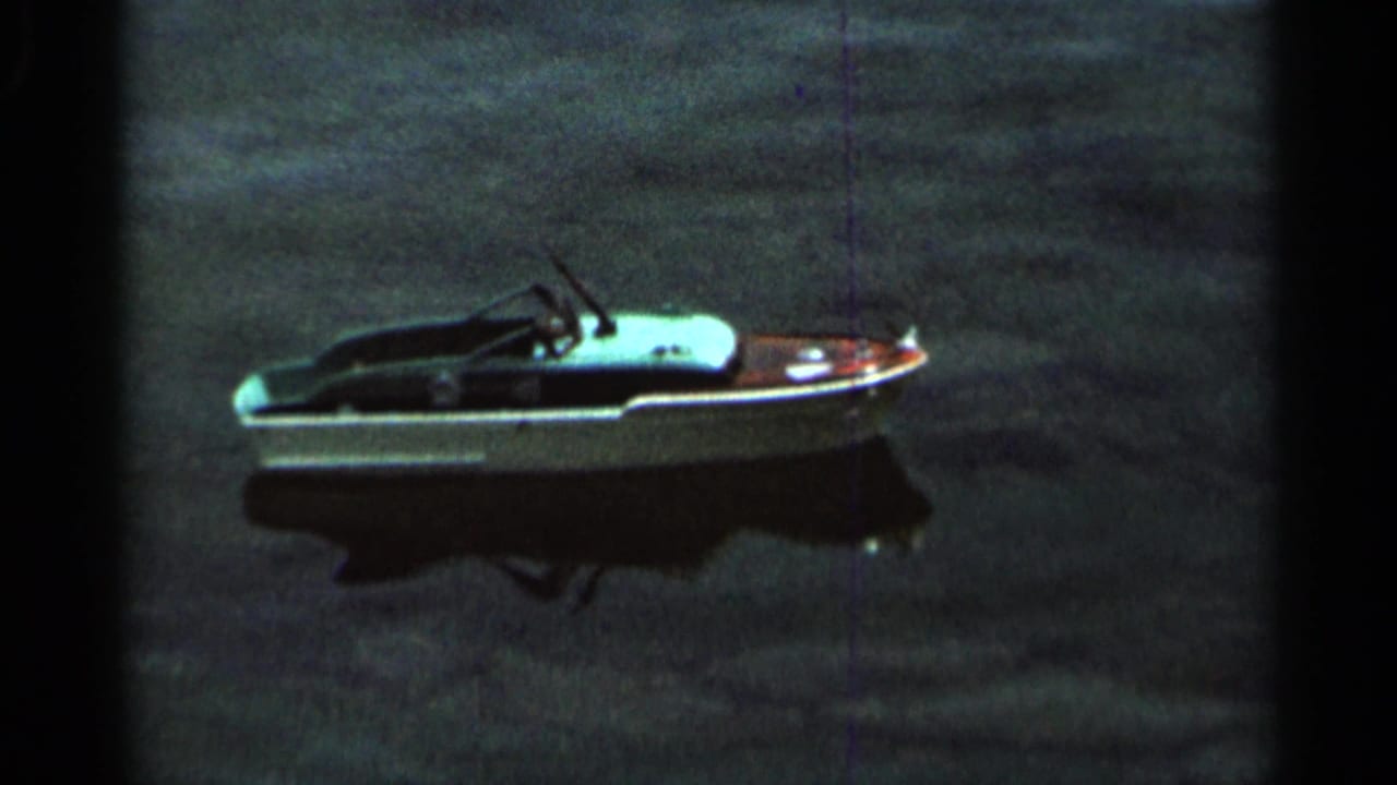 Small white toy boat floats on dark lake water with its reflection below.