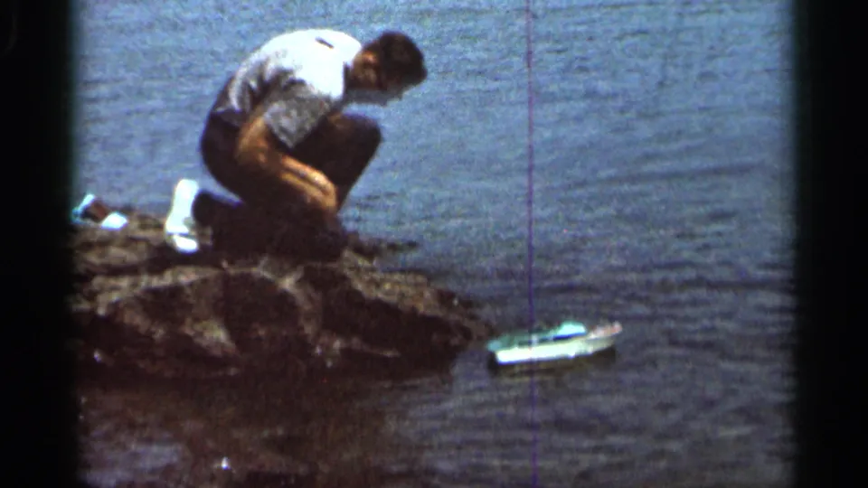 The man remains crouched on the rocks in the 1966 Hamel lakeside scene as the miniature boat moves into the water.