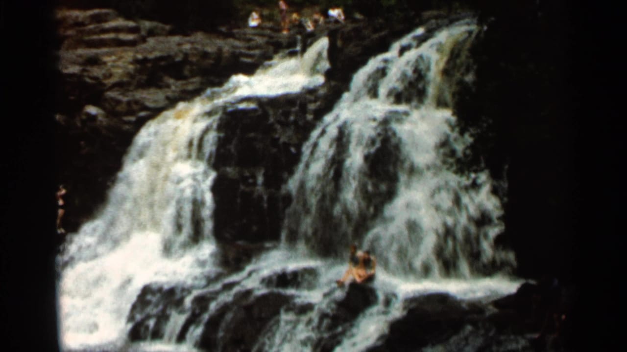 Wide view of the waterfall with a person seated on a rock ledge.
