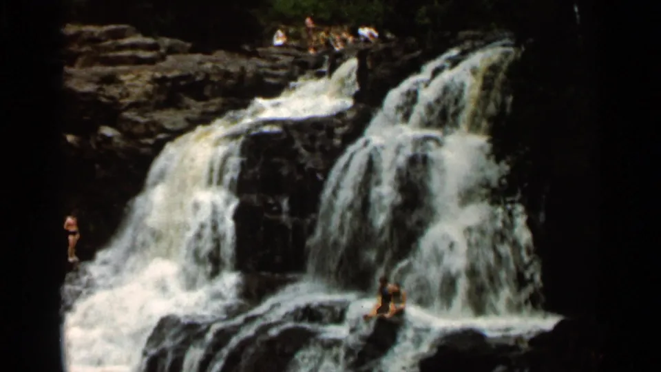 Home-movie frame from the 1966 Hamel, Minnesota clip showing people on rocks around a multi-tier waterfall.