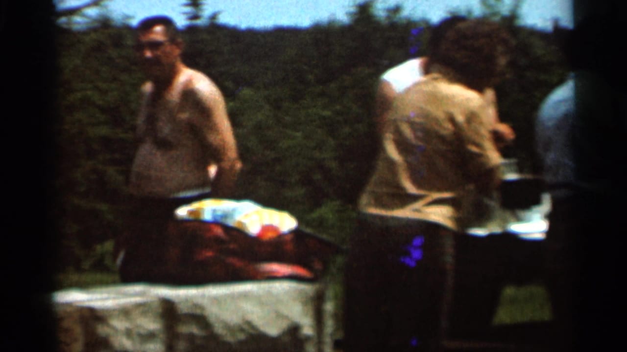 1966 Hamel, Minnesota 8mm frame showing men at a rustic outdoor barbecue setup beside trees and a colorful cooler.