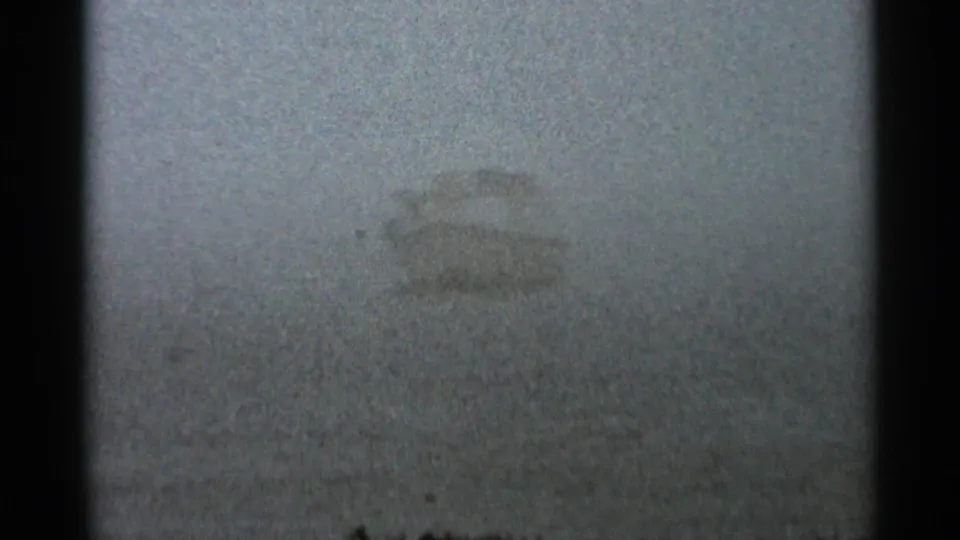 Foggy 1966 home-movie view of a small white boat form on water, softened by grain and low contrast.