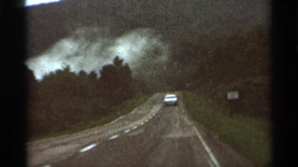 The final 1966 8mm frame shifts to a rural wooded road with a car driving ahead under overcast sky.