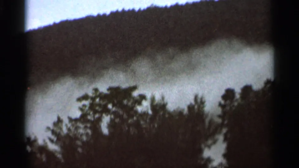 Final 1966 8mm frame showing smoke drifting across treetops below a dark wooded hillside near Hamel, Minnesota.