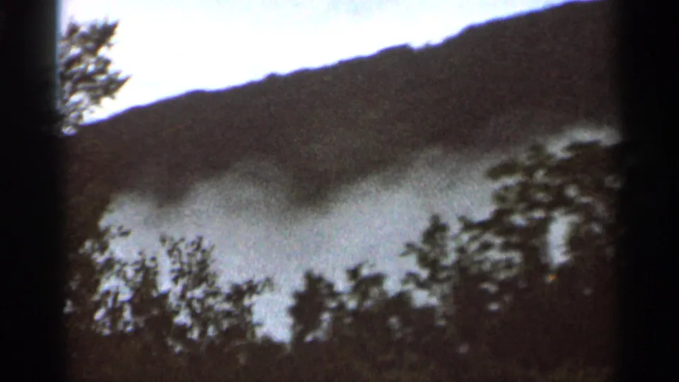 1966 Hamel, Minnesota home-movie frame showing fog over a wooded hillside, partly obscured by dark frame-edge shadows.