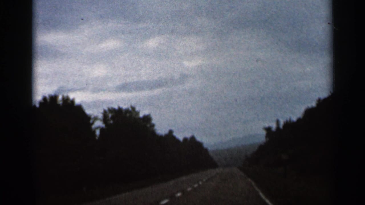 1966 Hamel, Minnesota 8mm frame showing a rural road receding between tree lines beneath an overcast sky.
