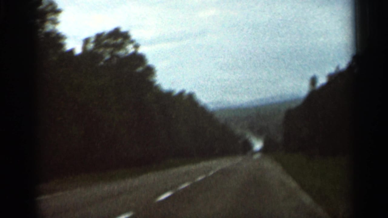 Tree-lined highway with a bright strip of road visible between wooded slopes.