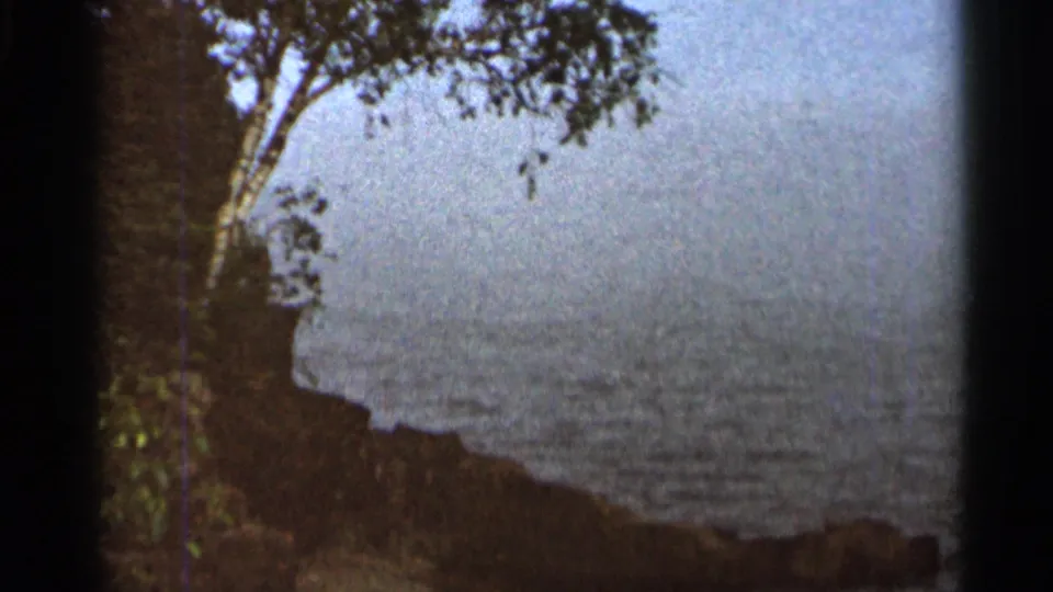 1966 8mm scenic frame showing water, tree branches, and a shadowed shoreline during the Cascade Falls outing.