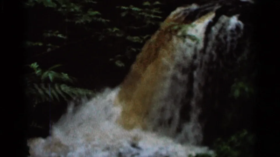 1966 Hamel, Minnesota 8mm frame showing water pouring over a rocky ledge into foamy white flow, surrounded by dark greenery.