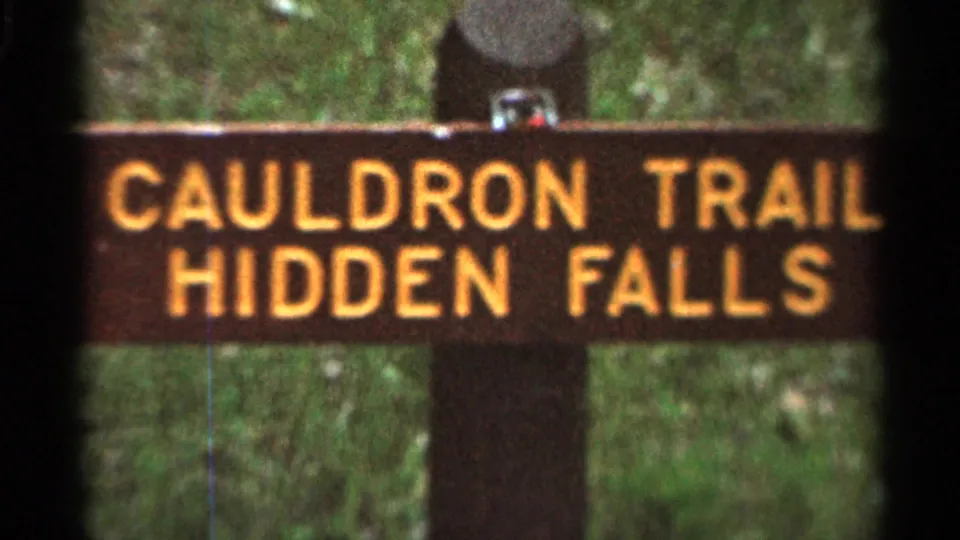 1966 8mm frame from Hamel, Minnesota, showing a wooden sign with yellow letters reading CAULDRON TRAIL HIDDEN FALLS.