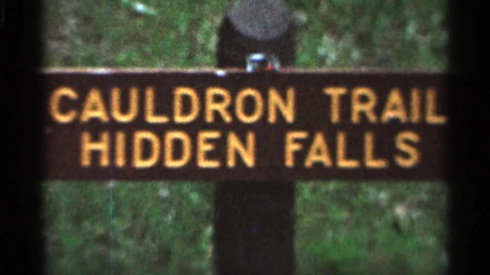 1966 Hamel, Minnesota frame with a close view of the CAULDRON TRAIL HIDDEN FALLS sign against green vegetation.