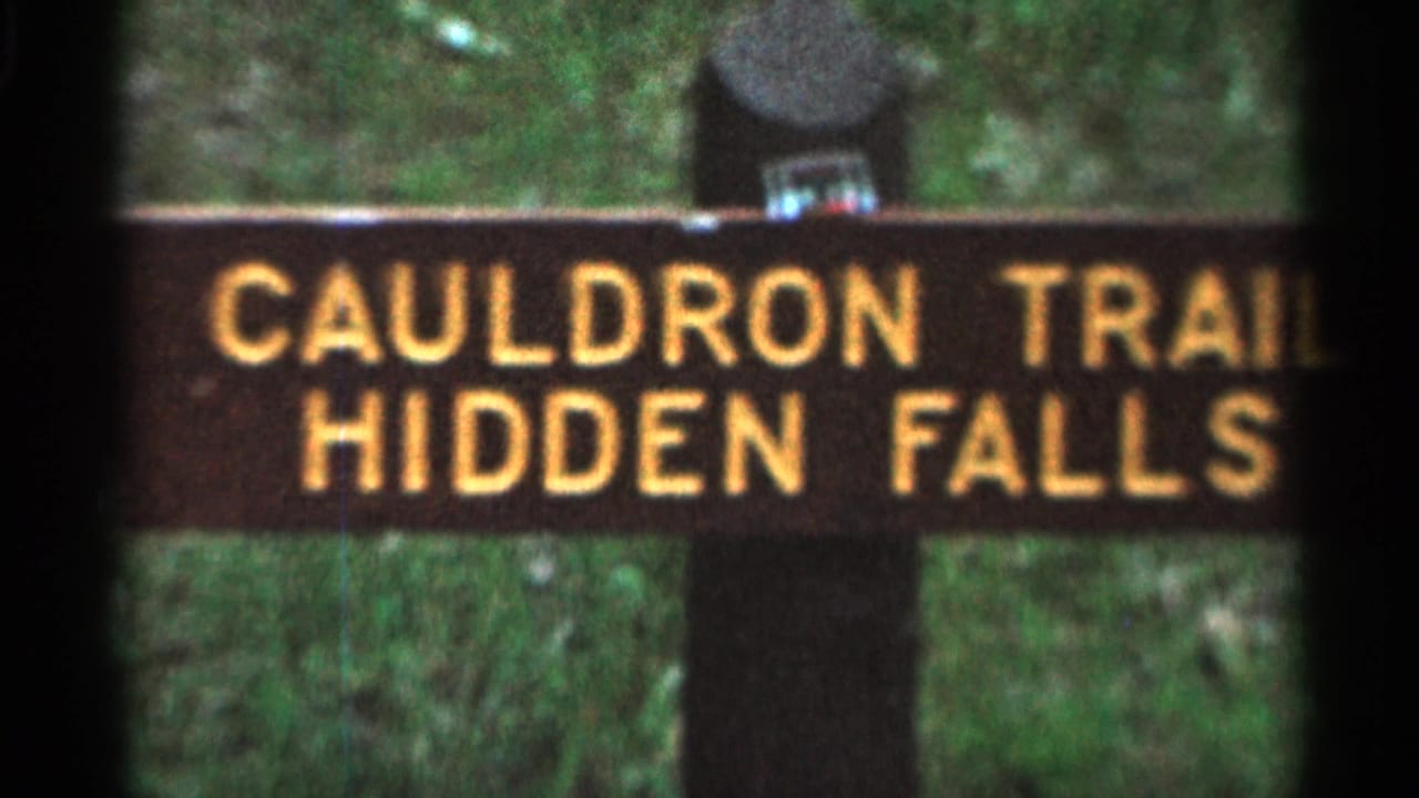 Wooden sign reading Cauldron Trail Hidden Falls against green foliage.