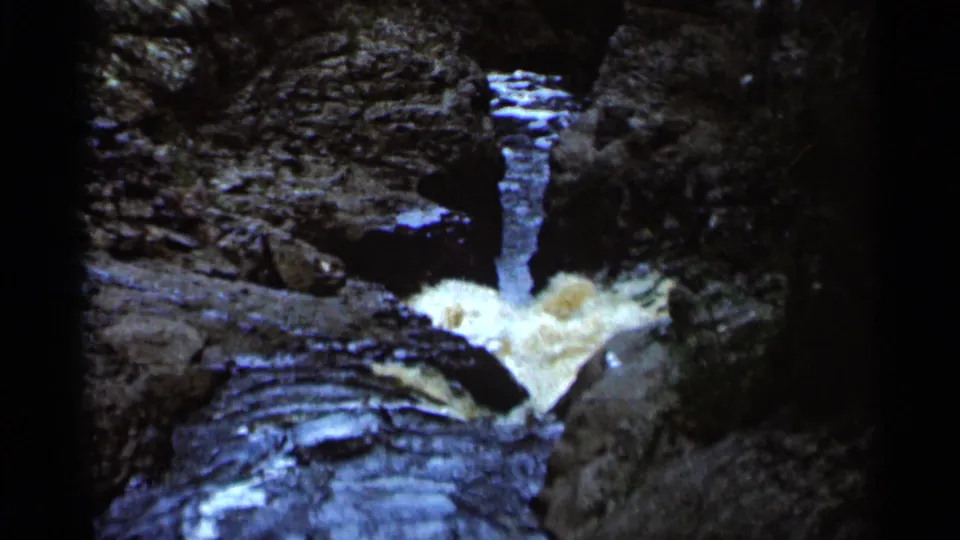 1966 8mm frame from Hamel, Minnesota, showing white water moving through a narrow rocky channel in a wooded setting.