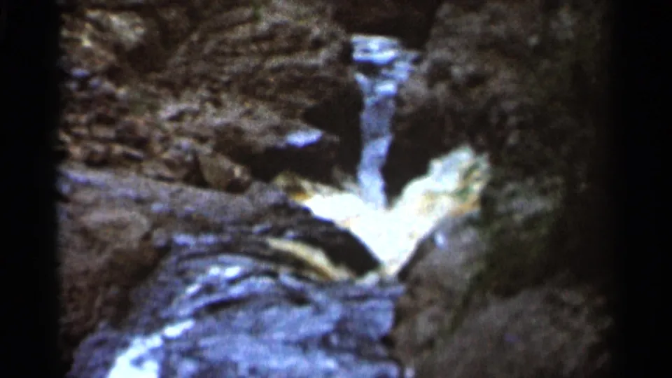 1966 Hamel, Minnesota frame showing a small stream cascade flowing over rocks, softened by grain and dim 8mm exposure.