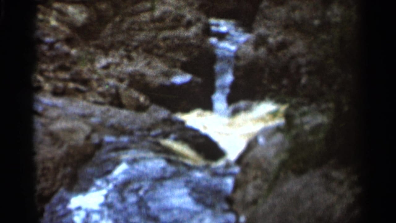 1966 8mm home-movie frame from Hamel, Minnesota showing a narrow cascade flowing through dark rocky banks.