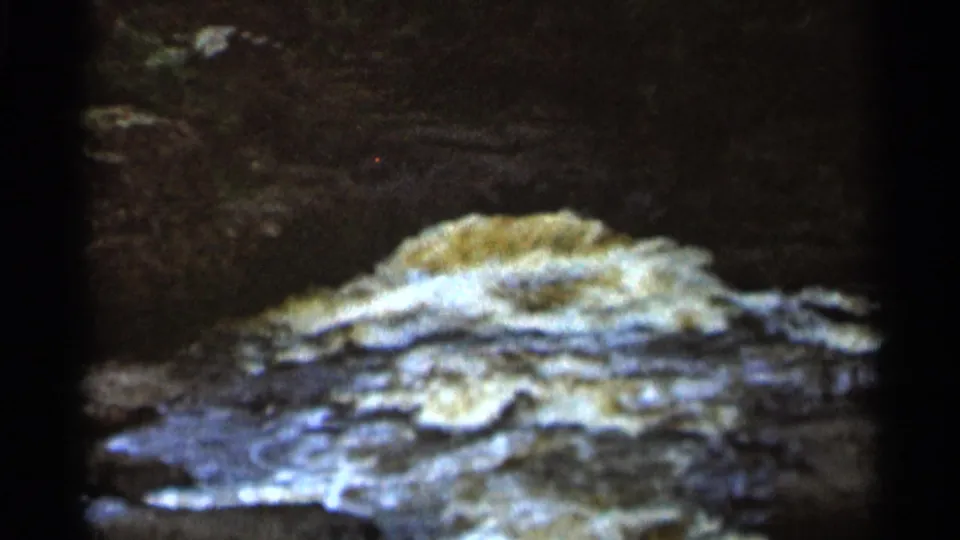 1966 8mm home-movie frame from Hamel, Minnesota, showing muddy rapids and white foam against dark rock edges.