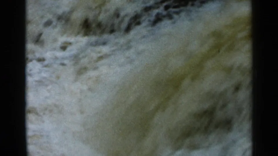 1966 8mm frame showing fast muddy water and darker ripple patterns, likely part of the same turbulent rapids sequence.
