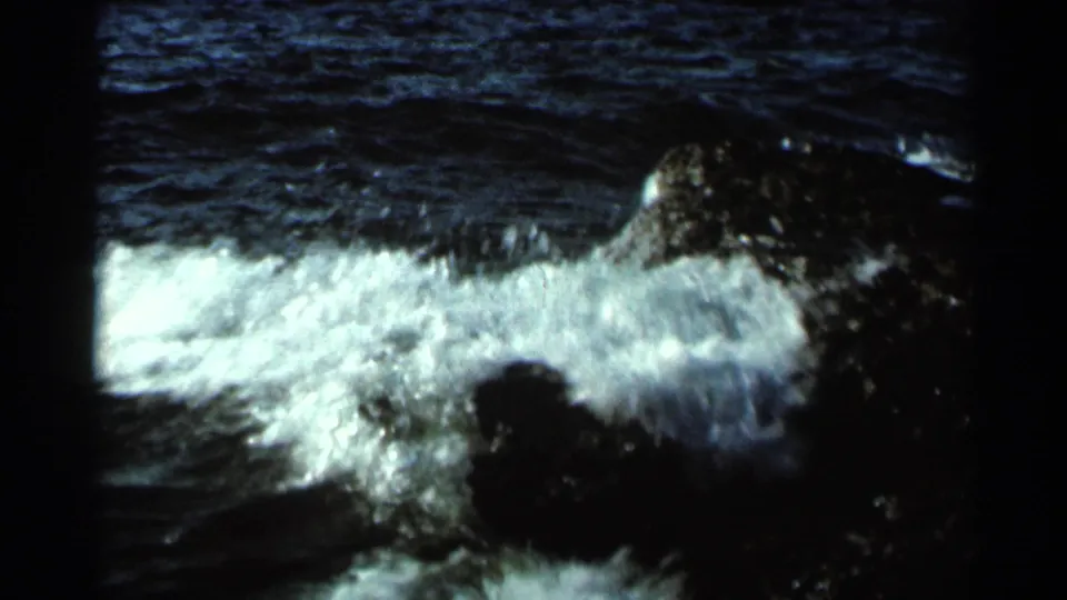 1966 Hamel, Minnesota 8mm frame showing darker stream water, white foam, and a shadowed rock or bank area.