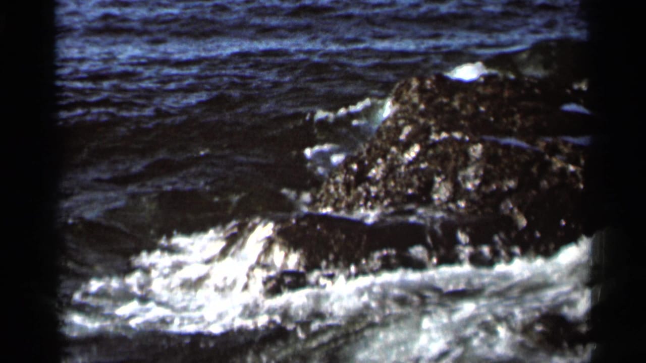 1966 8mm home-movie frame showing lake water foaming against dark jagged rocks near Hamel, Minnesota.