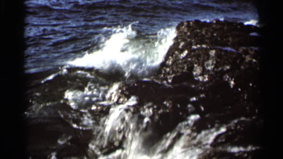 1966 8mm frame of a lake wave bursting into white spray over dark shoreline rocks in the Hamel, Minnesota clip.