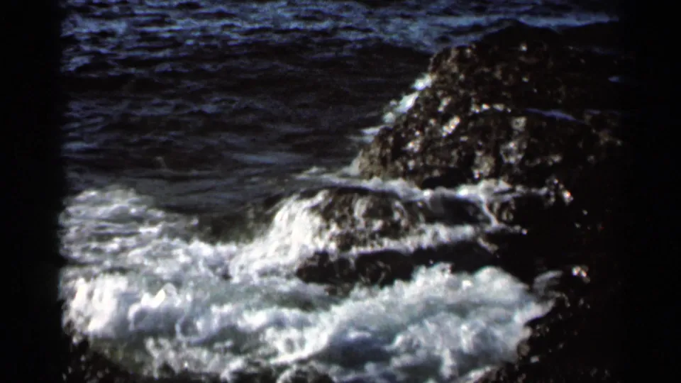 1966 8mm home-movie frame showing foamy lake water washing around a dark rock formation near Hamel, Minnesota.