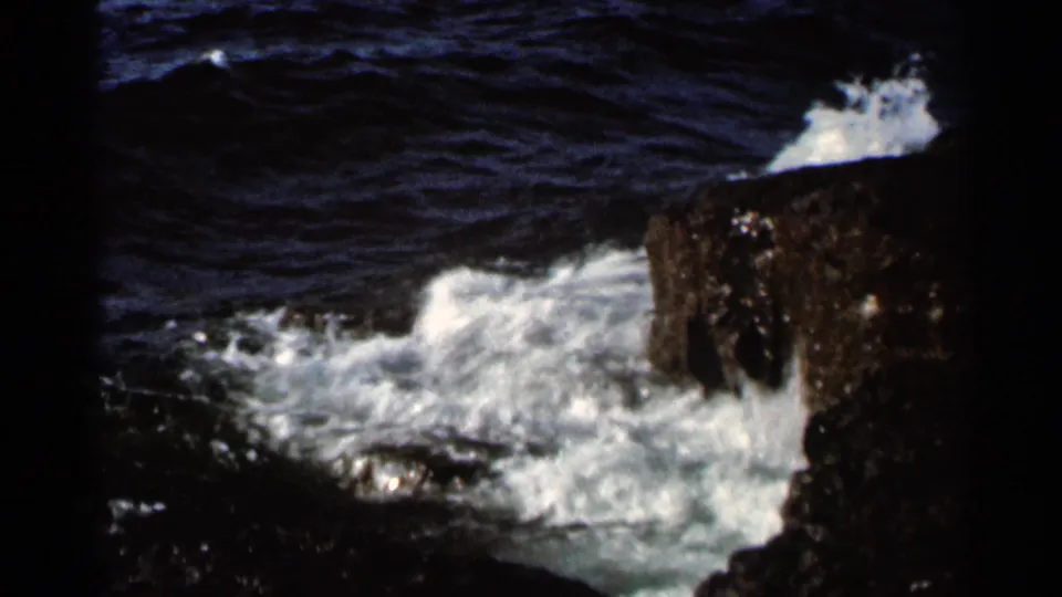 1966 8mm frame showing a burst of white lake water against a dark rock edge in the Hamel, Minnesota shoreline footage.