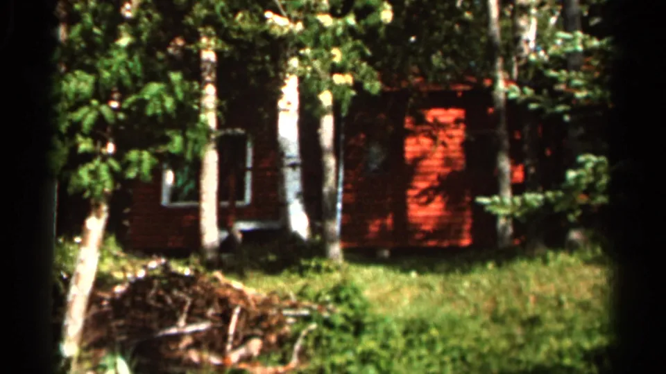 1966 8mm frame from Hamel, Minnesota showing a red cabin or house set back among tall trees and sunlit grass.