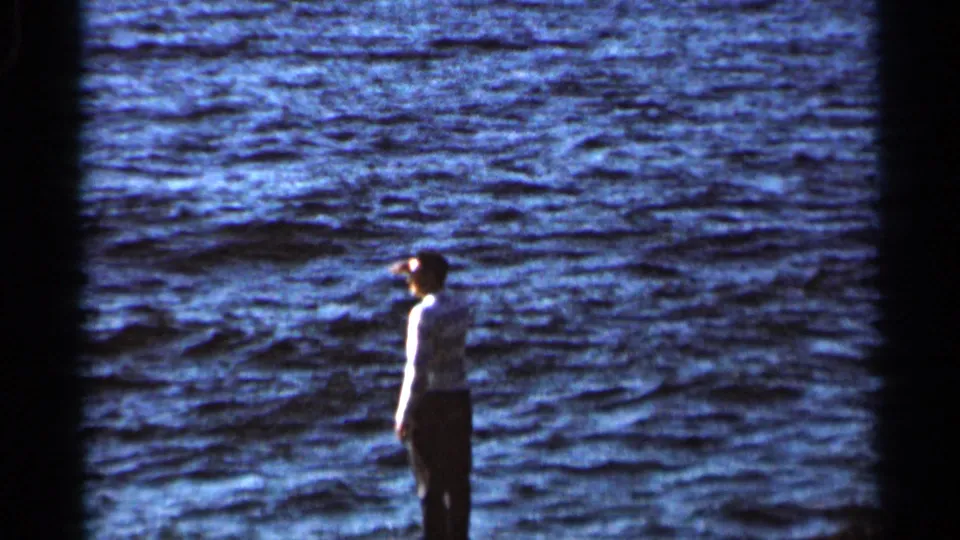 Adult man in a light shirt stands in profile beside wind-ruffled blue water in this 1966 8mm home-movie frame.