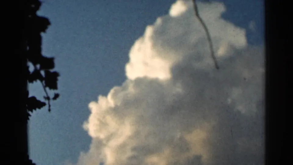 1966 Hamel, Minnesota 8mm frame with a large white cloud mass, blue sky, and silhouetted leaves or branches along the left border.