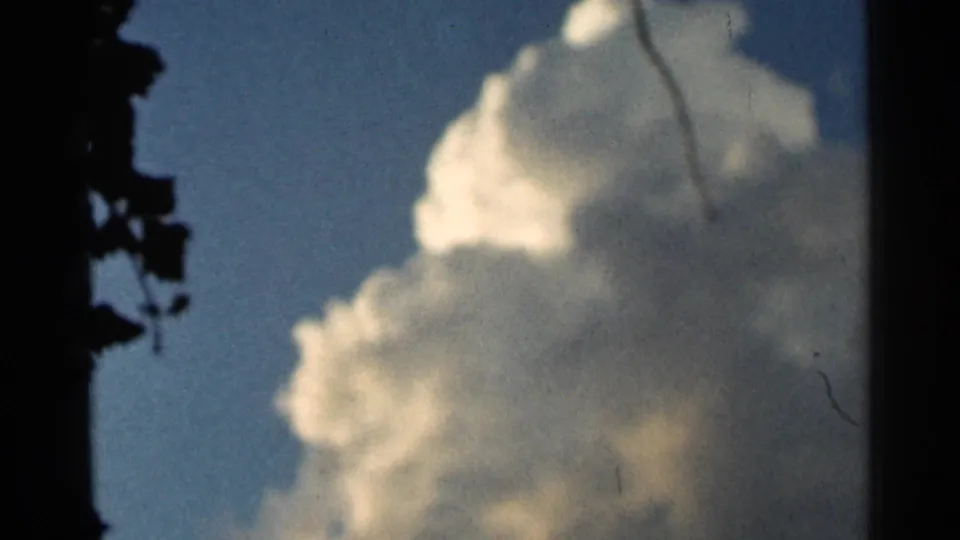 1966 Hamel, Minnesota 8mm frame showing a tall sunlit cumulus cloud, blue sky, dark edge foliage, and small film scratches.