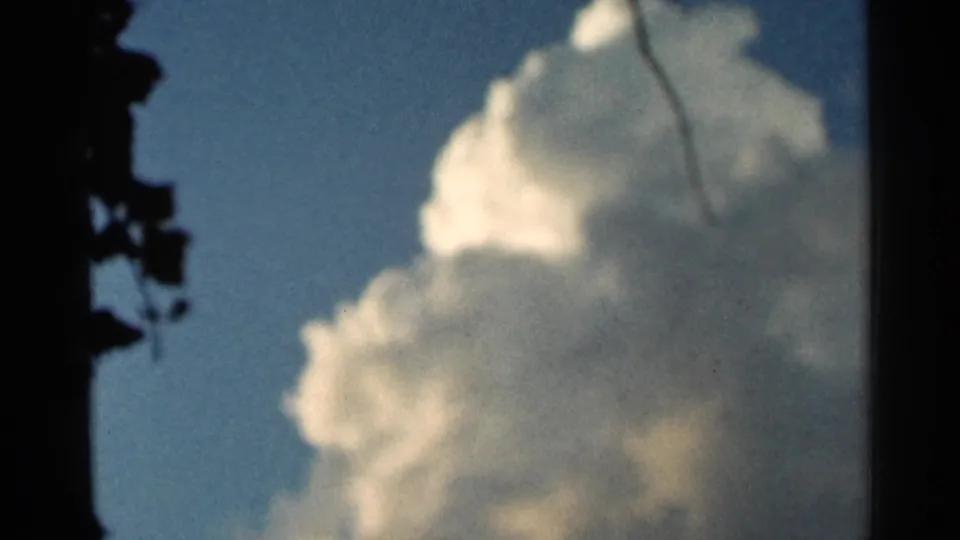 1966 Hamel, Minnesota 8mm frame of a soft sunlit cloud mass in blue sky, with a dark branch or wire-like line near the upper area.