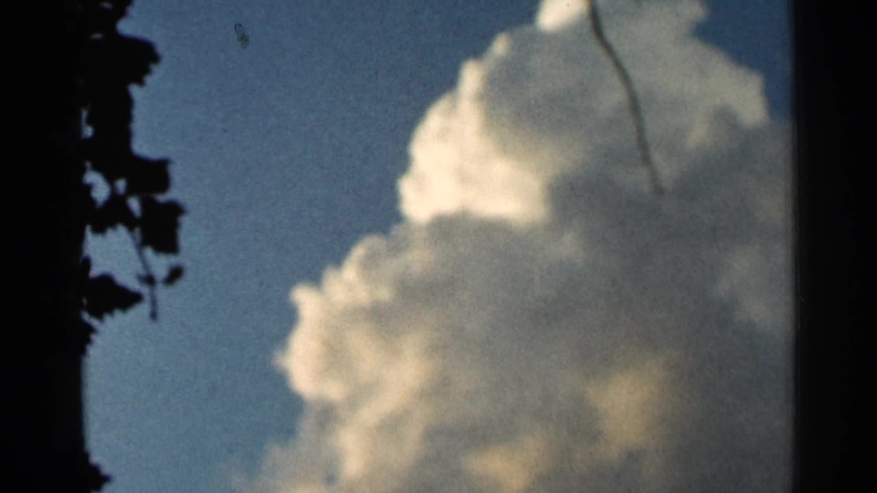 1966 Hamel, Minnesota 8mm frame showing a tall white cumulus cloud in blue sky, bordered by dark tree foliage and film edge shadow.