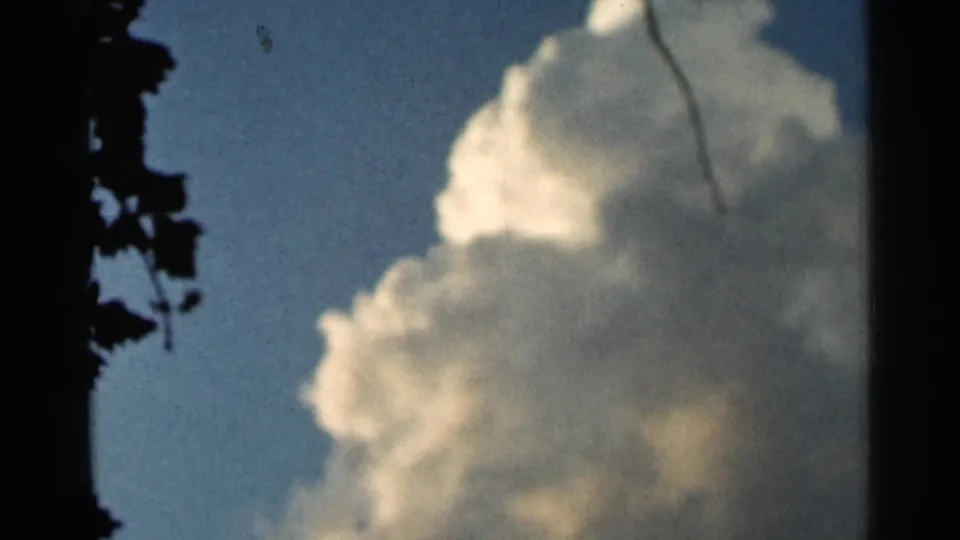 1966 Hamel, Minnesota 8mm frame showing a tall white cumulus cloud in blue sky, bordered by dark tree foliage and film edge shadow.