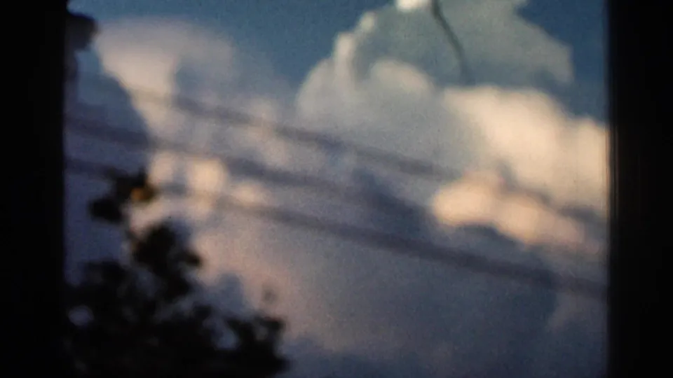 1966 Hamel, Minnesota 8mm frame with soft cumulus clouds, horizontal utility lines, and dark tree silhouettes near the frame edges.